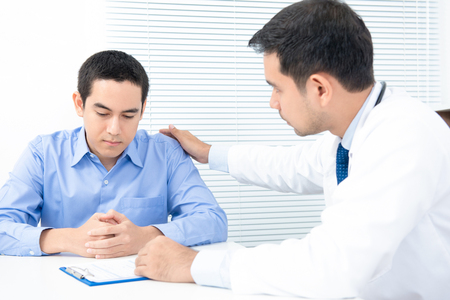 Doctor comforting depressed male patientの写真素材