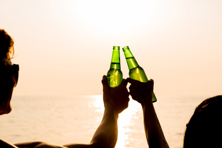 Couple clanging bottles of beers, celebrating on holiday at the beach in summer sunsetの写真素材