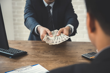 Businessman giving money, Japanese yen banknotes, to his partner while making contract - loan, bribery and corruption conceptsの写真素材