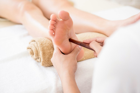 Professional therapist giving traditional thai foot massage with stick to a woman in spaの写真素材