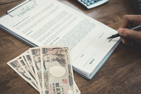 Businessman signing contract with money, Japanese yen banknotes, on the table - loan, bribery and corruption conceptsの写真素材