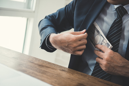 Businessman putting money, Japanese  yen banknotes, into his suit pocket - bribery and corruption conceptの写真素材