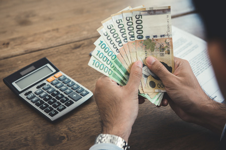 Hands of businessman holding money, South Koren won banknotes, at working deskの写真素材