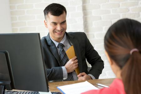 Businessman putting envelope into his suit pocket while making an agreement at working deskの写真素材