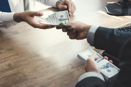 Businessman giving money to partner at working desk - loan, bribery and corruption conceptsの写真素材