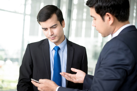 Two businessmen looking at smartphone and discussing at building hallwayの写真素材