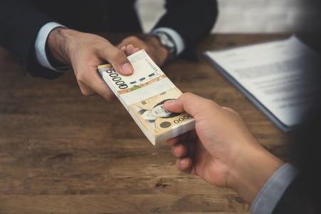 Businessman giving money, South Korean won banknotes, to his partner at the deskの写真素材
