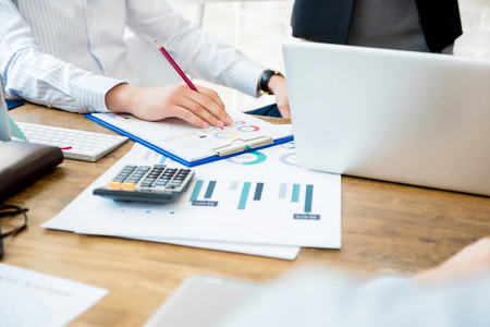 Businesspeople at working desk with financial graph documents, notebook computer and calculatorの写真素材