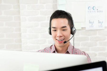 Casual Asian businessman wearing microphone headset working in the office as a telemarketing...