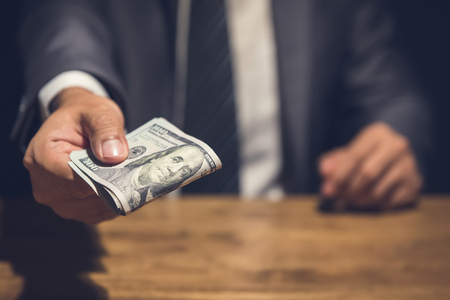 Dishonest businessman secretly giving away money in the dark - bribery, scam and venality conceptsの写真素材