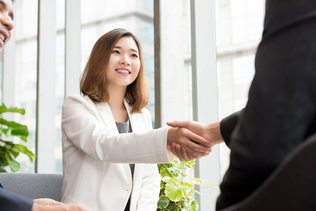 Smiling cheerful Asian business woman leader making handshake with a businessman in office loungeの写真素材