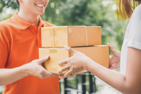 Smiling delivery man in orange uniform delivering parcel box to a woman customer - courier service...