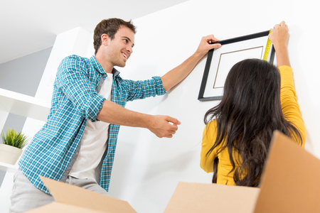 A couple decorating their new house by putting up photo frame and measuring the distnace with a measuring tapeの写真素材