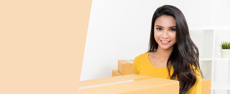 Beautiful Asian woman carrying a box moving into her new home - horizontal web banner with copy space on the leftの写真素材