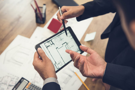 Real estate agent with client or architect team discussing a housing model and its blueprints digitally using a tablet computerの写真素材