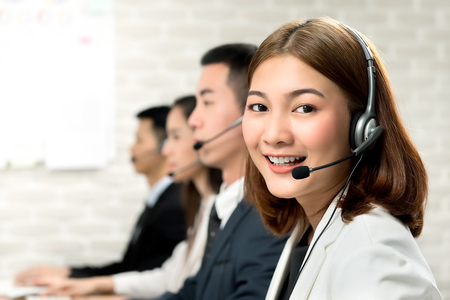 Smiling beautiful young Asian woman telemarketing customer service agent working in call center office with friendly and helpful attitudeの写真素材