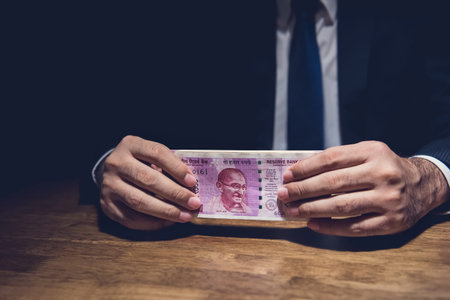 Anonymous businessman holding money, Indian Rupee currency, at the table in dark private room - ...