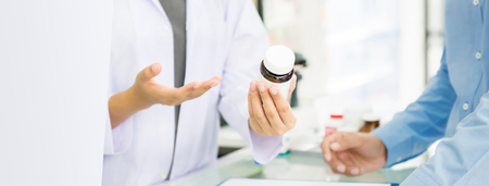 Female pharmacist holding medicine bottle giving advice to customer in chemist shop or pharmacy - horizontal web banner with copy space on the leftの写真素材