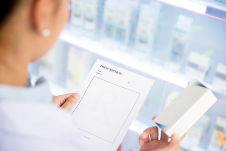 Female doctor or  pharmacist holding Rx prescription paper checking medicine in pharmacy (or chemist shop)の写真素材