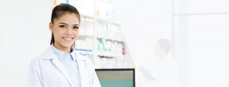 Smiling Asian female pharmacist in chemist shop or pharmacy - panoramic web banner with copy spaceの写真素材