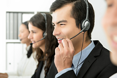 Smiling cheerful male telemarketing customer service agent with his team, call center job conceptの写真素材