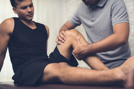 Therapist treating injured knee of athlete male patient in clinic - sport physical therapy conceptの写真素材