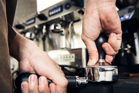 Barista making coffee,  pressing temper on portafilter before brewing, at cafe