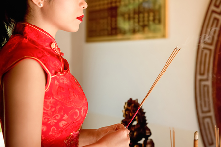Asian woman in red qipao dress praying with incense sticks during Chinese or Lunar new yearの写真素材