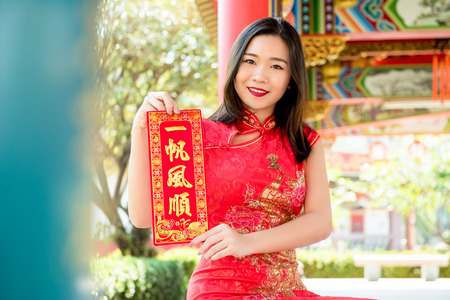 Smiling Asian woman in traditional red cheongsam qipao dress showing Chinese New Year greeting text sign said "everything will be good"の写真素材