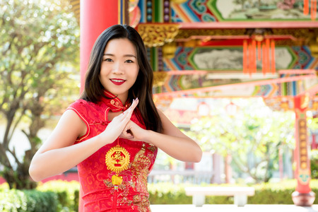 Smiling Asian woman in traditional red cheongsam qipao dress making salute with Chinese new year greeting sign in hand said "happiness and good fortune"の写真素材