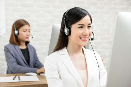 Beautiful smiling Asian businesswomen wearing headsets working in call center office as telmarketing customer service agentsの写真素材