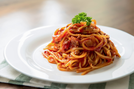 Delicious Italian bolognese meat spaghetti decorated with parsley on top in white dish at the tableの写真素材
