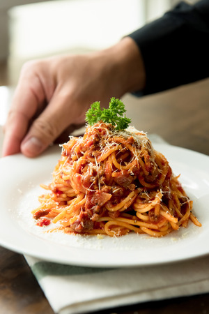 Delicious Italian bolognese meat spaghetti with parmesan cheese and parsley on top in white dish at the tableの写真素材