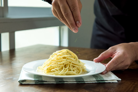 Chef seasoning Italian spaghetti with ground parsley on white dish at kitchen islandの写真素材