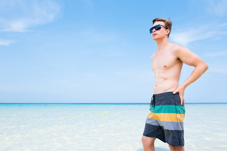 Shirtless handsome caucasian tourist man standing in clear seawater at the beach in Koh Samui Thailand during summer holidaysの写真素材