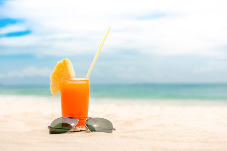 Refreshing cold tropical fruit punch drink with sunglasses in summer white sand beach backgroundの写真素材
