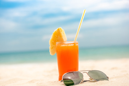 Refreshing cold tropical fruit punch drink with sunglasses in summer white sand beach backgroundの写真素材