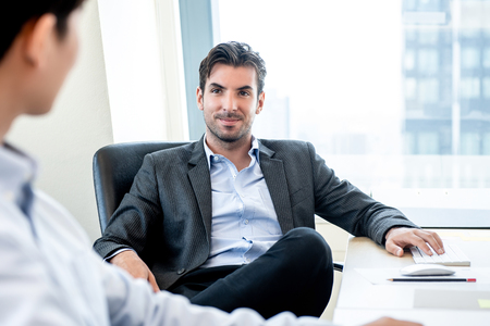 Handsome Hispanic businessman as a boss sitting in a chair listening to his colleague in the officeの写真素材