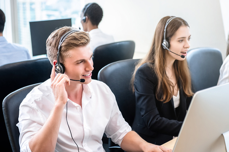 Friendly handsome man working in call center headquarters office with team as telemarketing customer service agentsの写真素材