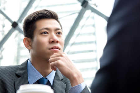 Young handsome Asian Chinese businessman concentrating on listening to his partner with eye contactの写真素材