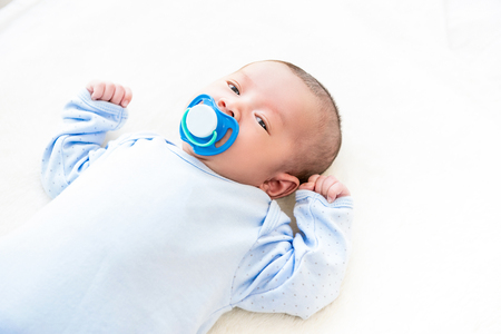 Adorable little newborn baby lying on white bed sheet with dummy in her mouthの写真素材