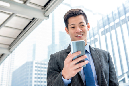 Young handsome Asian businessman  using mobile phone surfing internet searching for online information on the goの写真素材