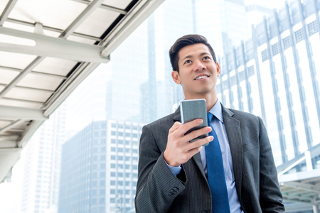 Young handsome Asian businessman  using mobile phone outdoors on the goの写真素材