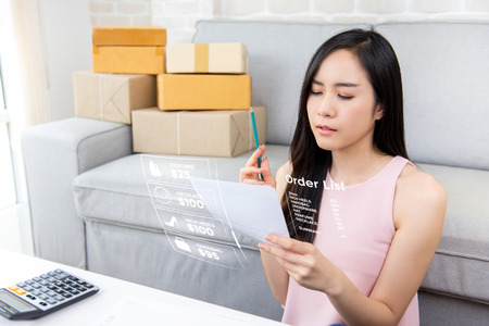 Young Asian woman entrepreneur or freelance online seller working at home checking orders preparing for delivery packages to customersの写真素材