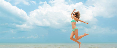Energetic happy woman in bikini jumping at the beach in summer blue sky banner background with copy spaceの写真素材
