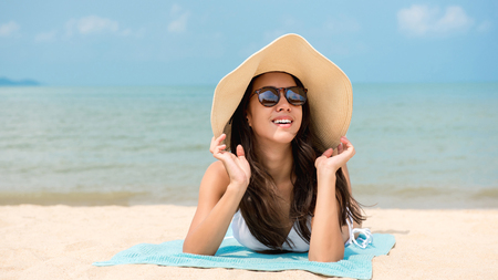 Young happy beautiful Asian woman lying on stomach taking a sunbath relaxing at the beach on summer vacationsの写真素材