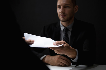 Businessman giving bribe money in white envelope to partner in a corruption scamの写真素材