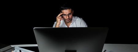 Serious Asian businessman  working late at night in the office looking at computer screen and thinking, panoramic bannerの写真素材