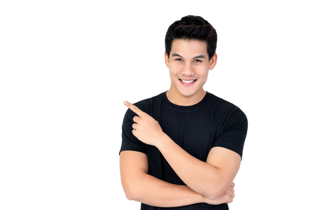 Isolated portrait of  happy smiling Asian man wearing casual black t-shirt pointing hand to empty space aside studio shot white backgroundの写真素材