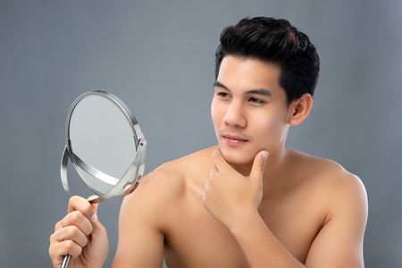 Beauty portrait of shirtless young handsome Asian man looking at his face in the mirrorの写真素材